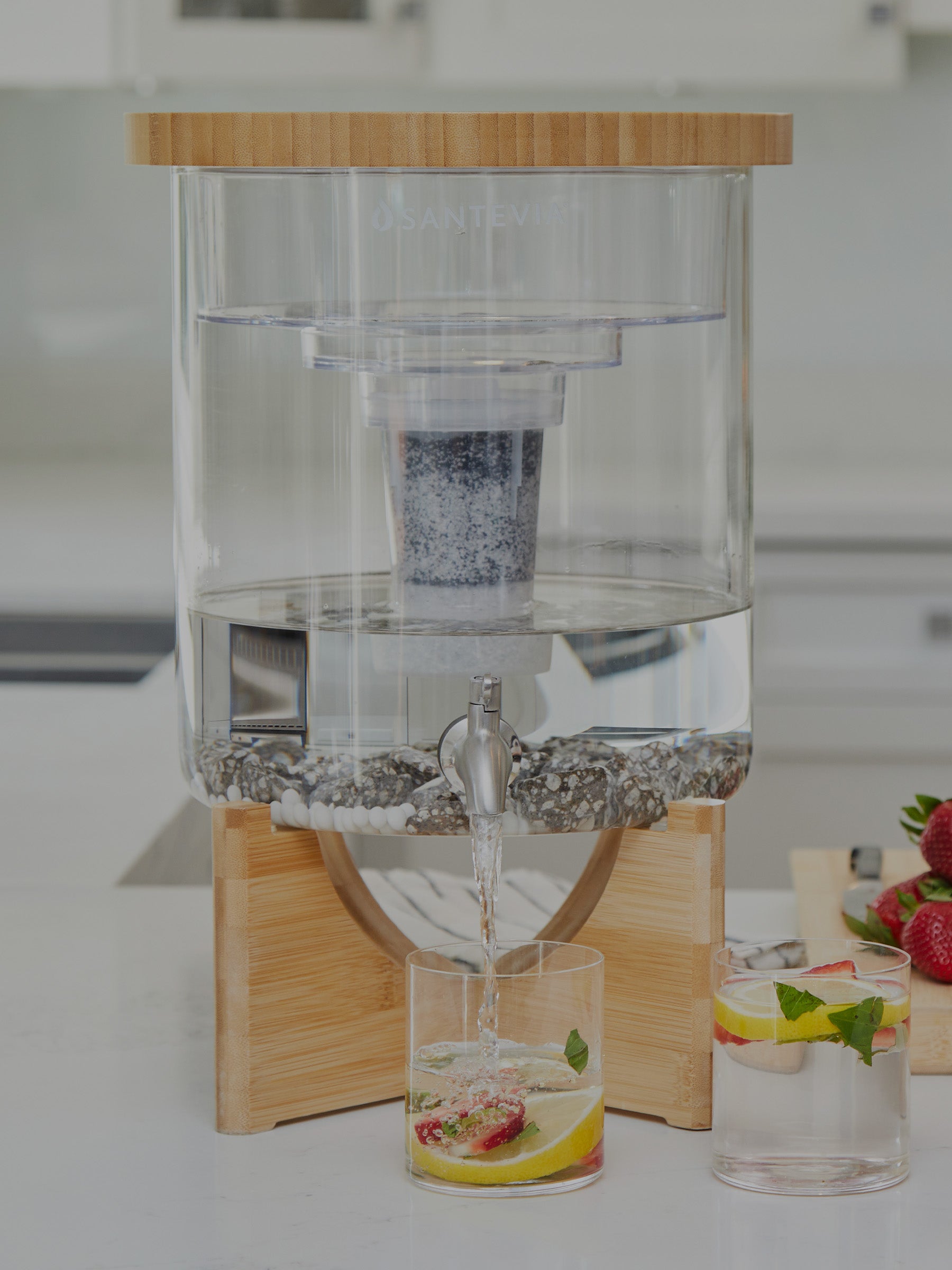 Clear glass drink dispenser with wooden base on a kitchen counter