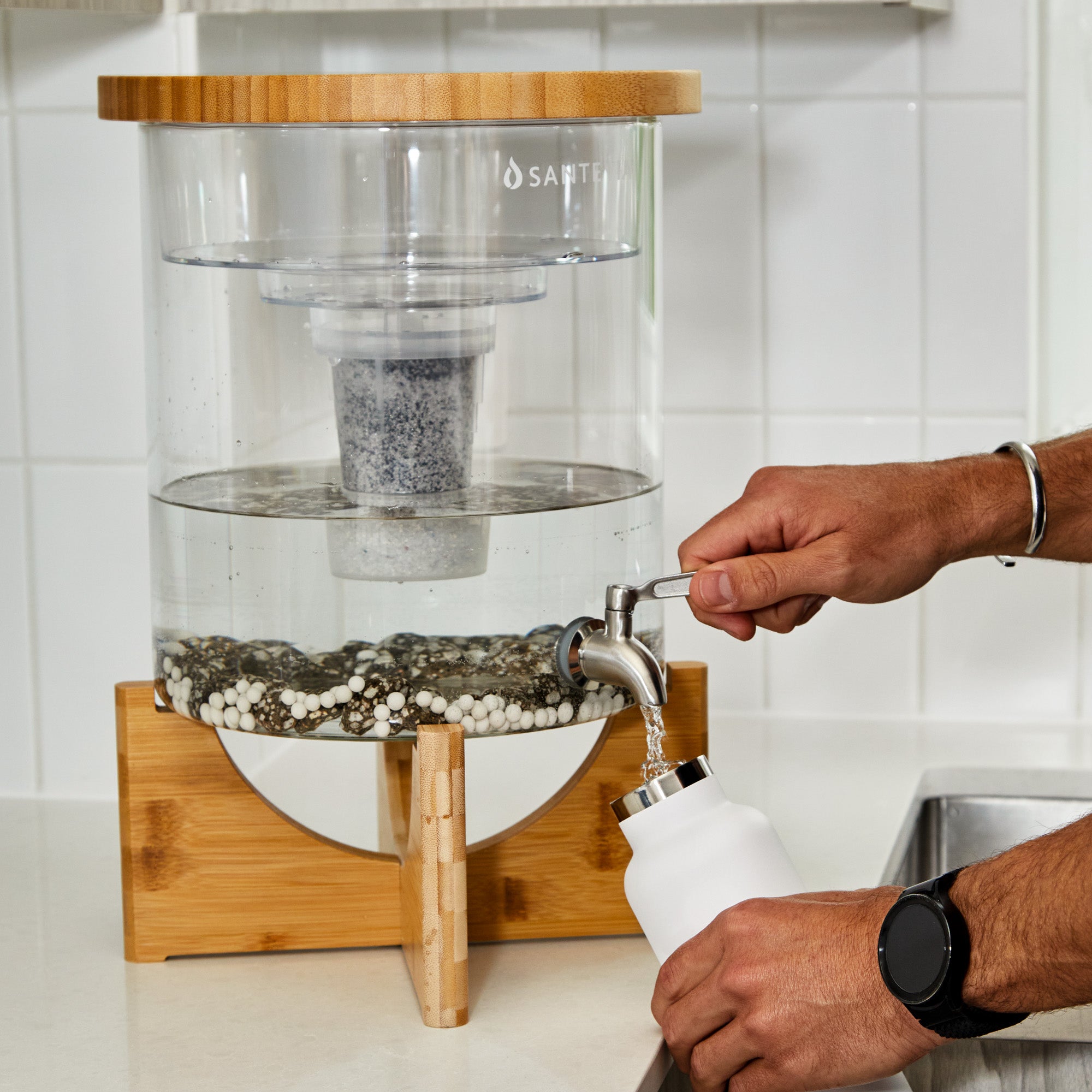 Person filling a white bottle with water from a Santevia water filter.