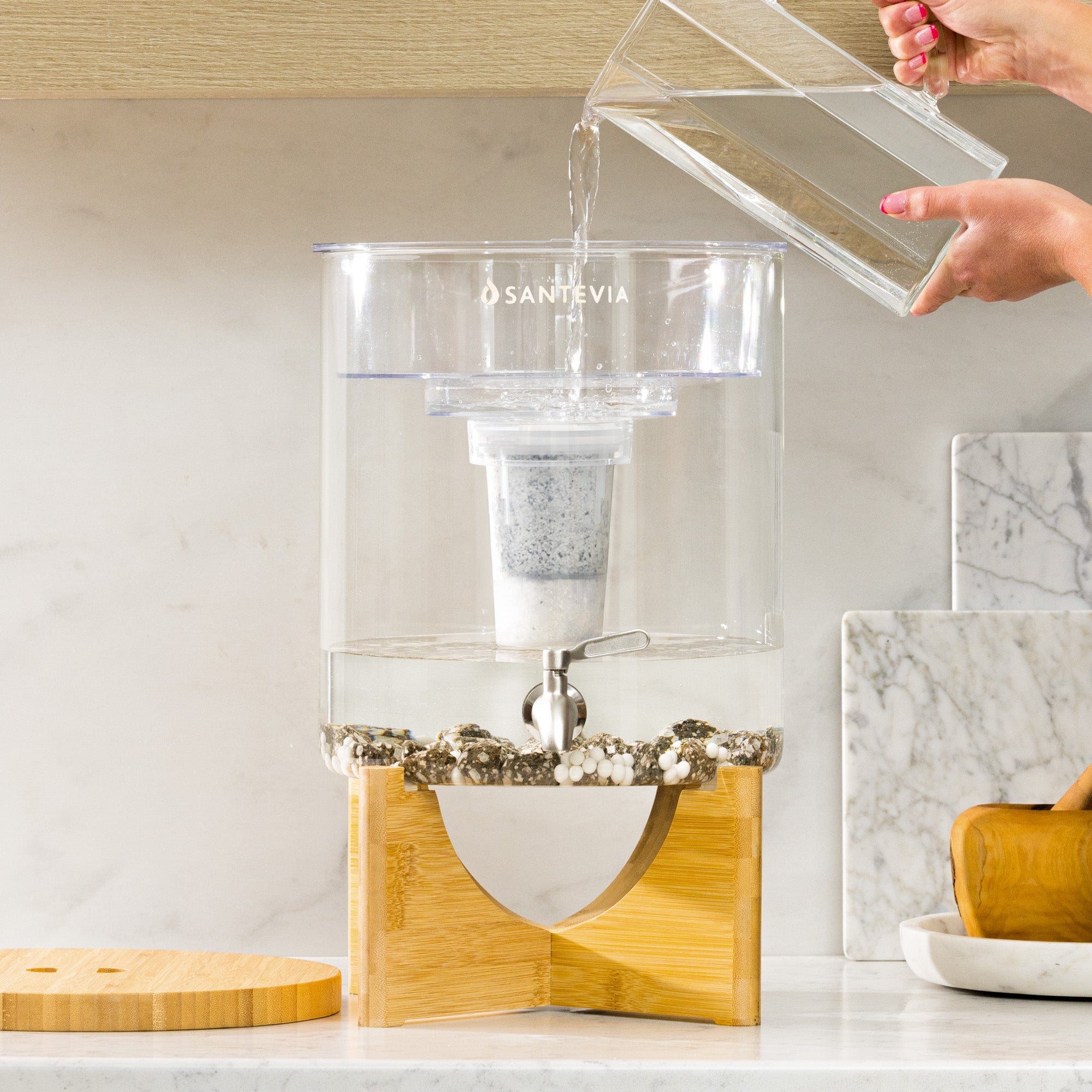 Santevia water filter on a kitchen counter with a hand holding a clear container above it.