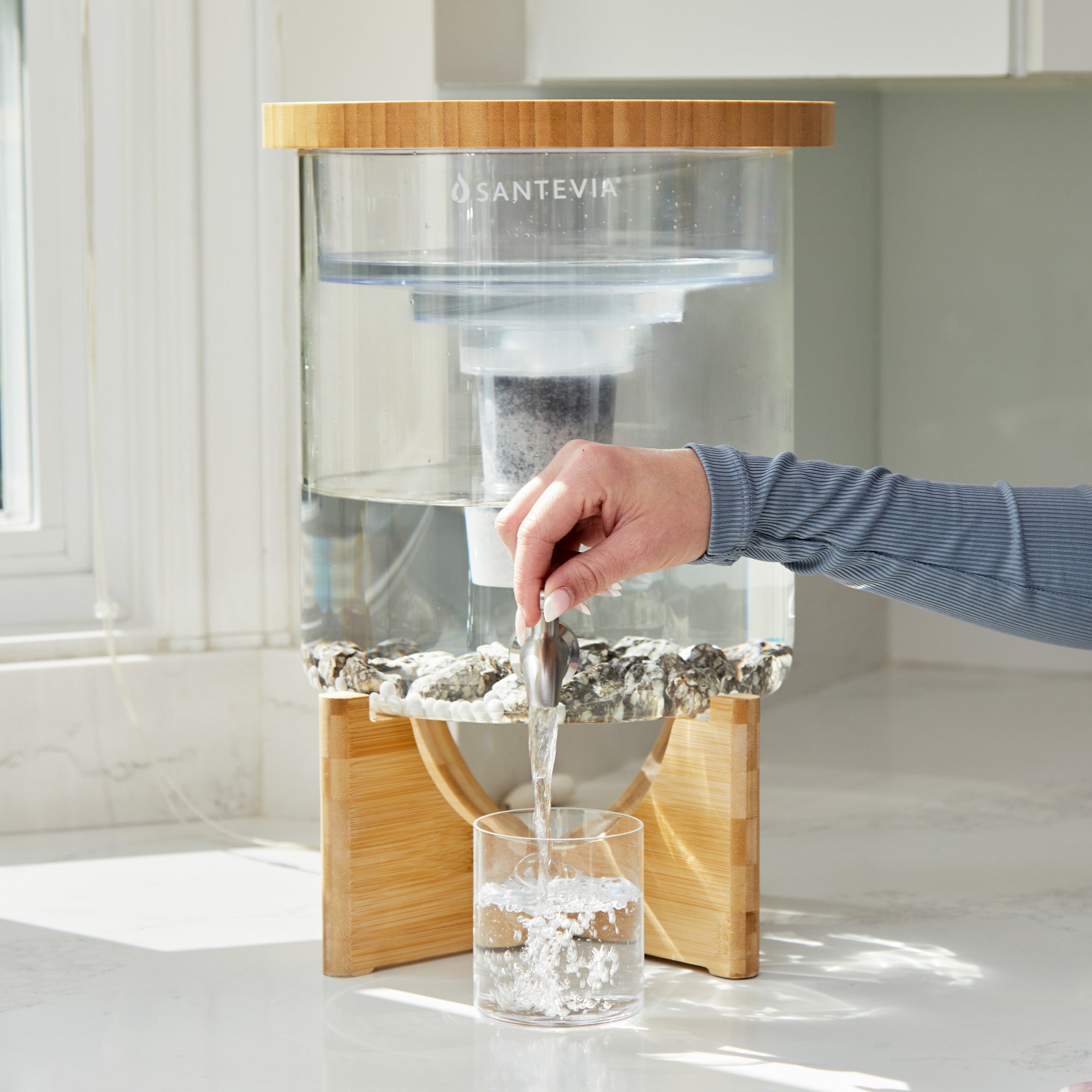 Person using a Santevia water filter to pour water into a glass on a kitchen counter.